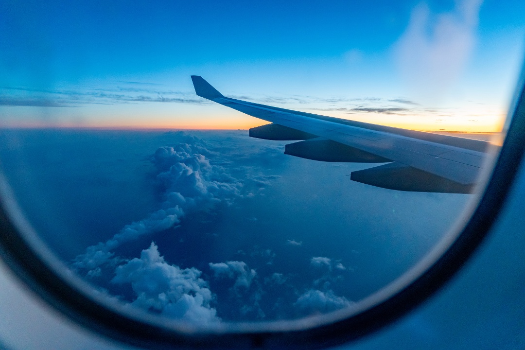looking out an airplane window, seeing the wing flying above the clouds