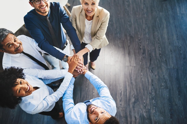 executive leaders look up at the camera as they huddle up with their hands